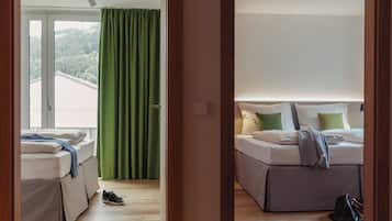 A hotel room with a bed, a window with curtains, a door, and a view of a forested area.