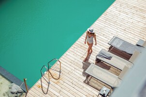 Una terraza de madera con piscina, sillas de descanso y un trampolín.