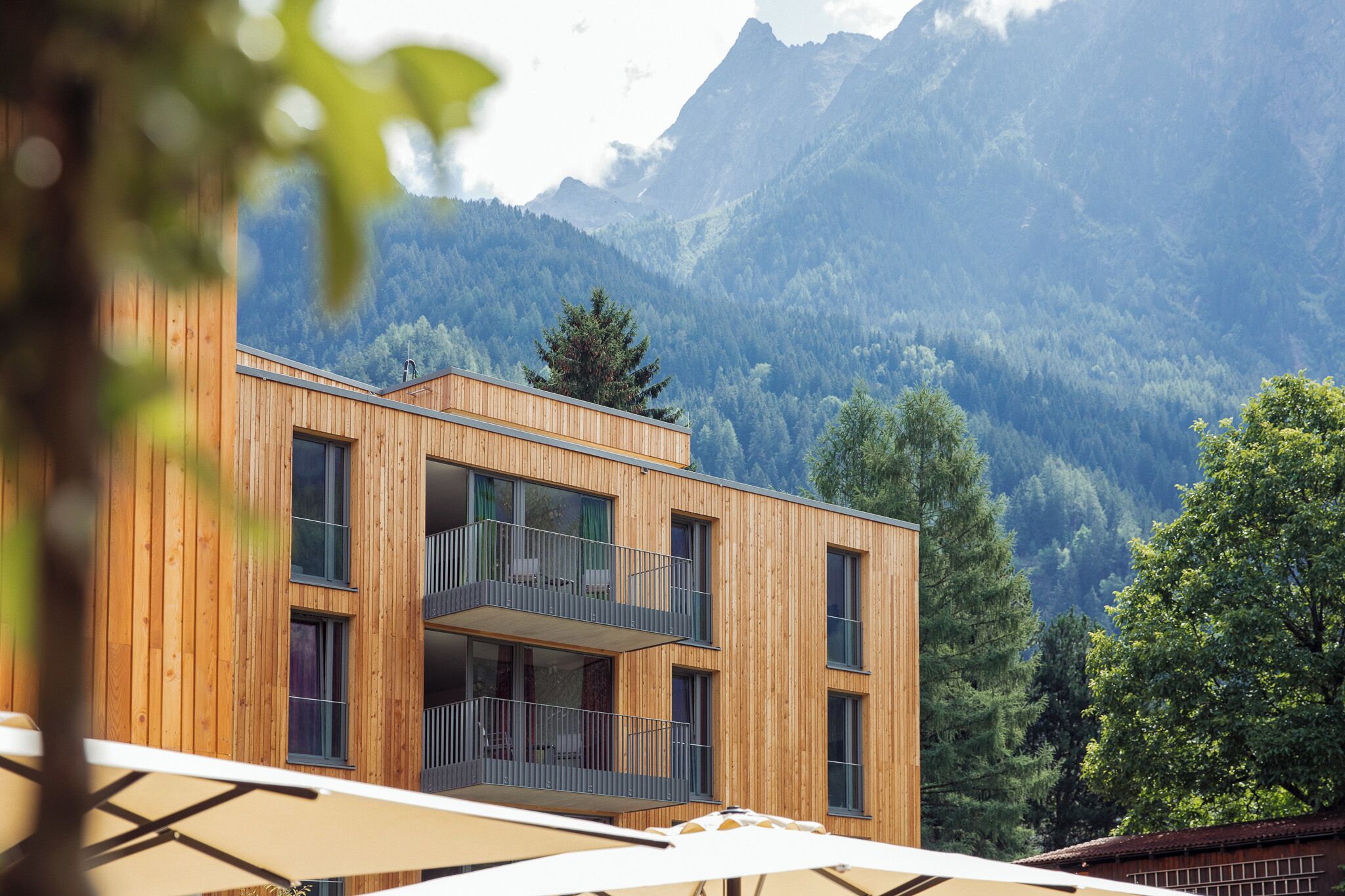 Ein modernes Holzgebäude mit Balkonen vor einer Bergkulisse.