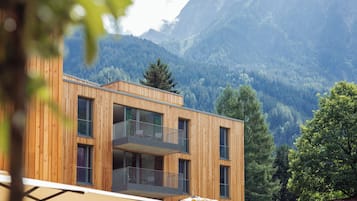 Ein modernes Holzgebäude mit Balkonen vor einer Bergkulisse.