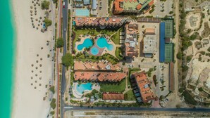 Vista aérea de un resort con varias piscinas, una playa y un estacionamiento.