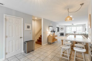 A modern kitchen with a central island, white bar stools, and a staircase leading to another room.