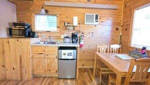 A compact kitchen with wooden cabinets, a stainless steel refrigerator, a coffee maker, and a window above the sink. - Sunset Ridge #2 at Rustic Ridge (Keystone)