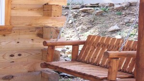 A wooden bench with a metal chain swing attached to a log cabin wall. - Sunset Ridge #2 at Rustic Ridge (Keystone)