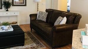 A living room with a brown leather sofa, a black ottoman, a white console table with a plant, and a ceiling fan. - Enjoy a Relaxing Getaway at our Cottage in Prescott Valley (Prescott Valley)
