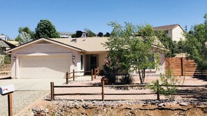 A single-story house with a garage, a small porch, and a fenced yard with a tree and a flower bush. - Enjoy a Relaxing Getaway at our Cottage in Prescott Valley (Prescott Valley)