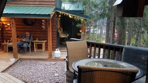 A wooden deck with outdoor seating, a covered area with a green roof, and a forested backdrop.