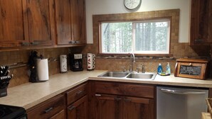 A kitchen with wooden cabinets, a double sink, a coffee maker, and a clock on the wall.