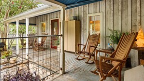Une véranda en bois avec des fauteuils à bascule et une table, un espace couvert avec un plafond bleu, et une vue sur les arbres et les fleurs.