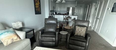 Una sala de estar con un sofá, dos sillones de cuero, una mesa de centro con conchas marinas, una mesita auxiliar y un cuadro en la pared.