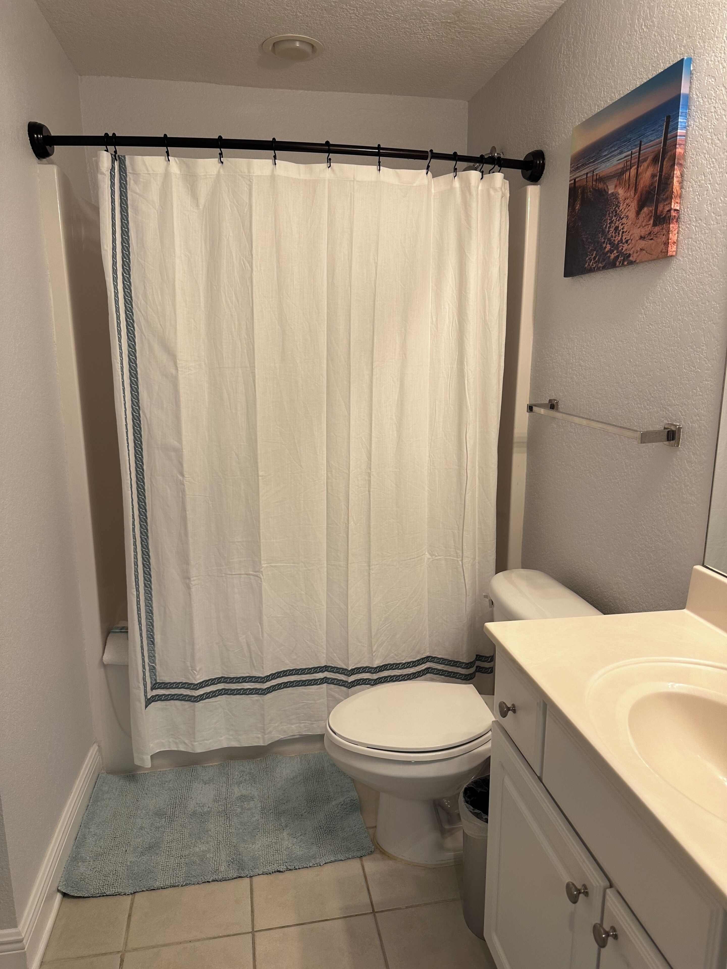 Une salle de bain avec un rideau de douche blanc, des toilettes, un lavabo et un porte-serviettes.