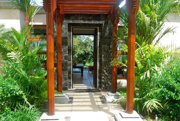 A stone archway leading to a pool area surrounded by lush greenery.