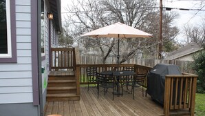 Una terraza de madera con una mesa, sillas, una parrilla y un toldo.