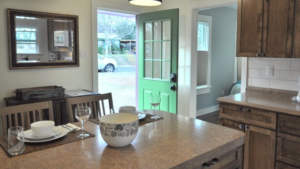 Una cocina con una puerta verde, una mesa de comedor con un bol y una copa de vino, y armarios de madera.