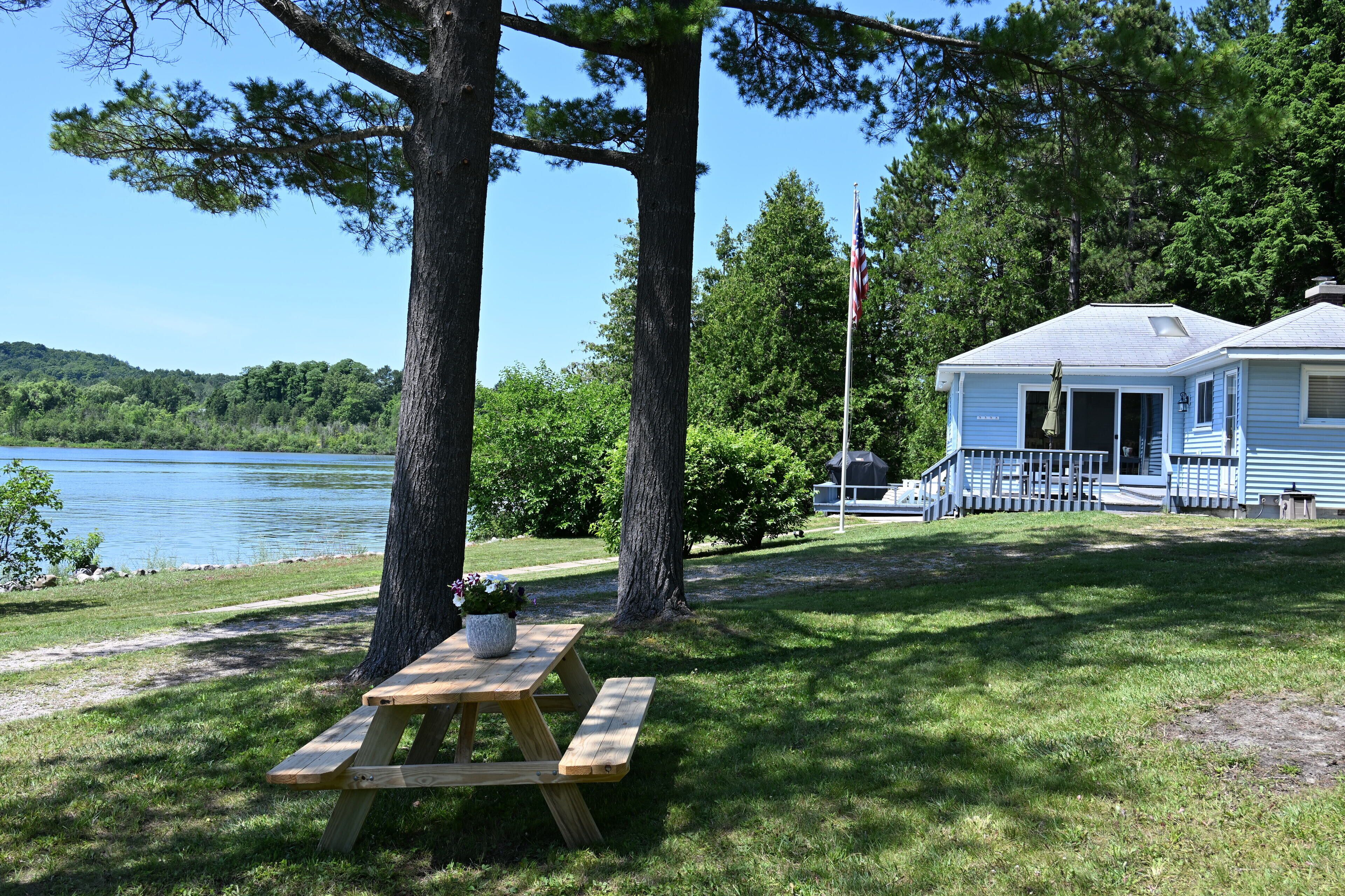 Een blokhut aan het meer, met een picknicktafel, omringd door bomen en uitzicht op het water.