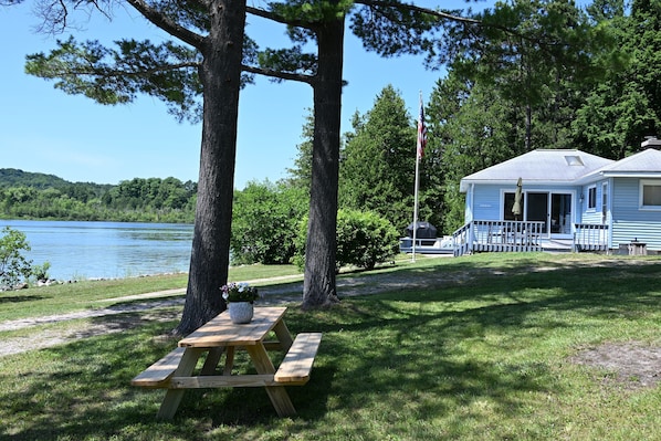 A lakeside cabin with a picnic table, surrounded by trees and a view of the lake.