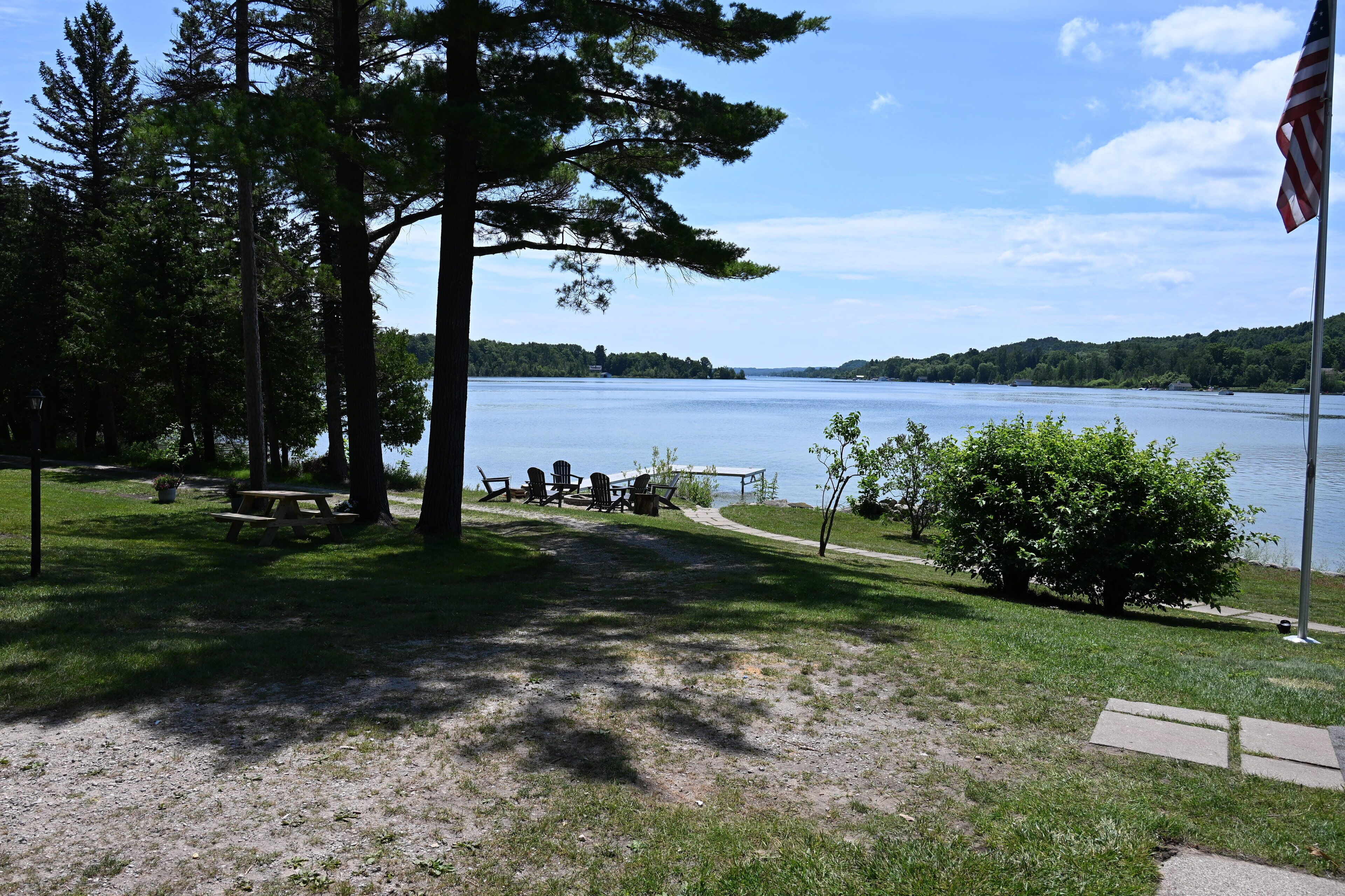 A lakeside park with picnic tables, chairs, and a flagpole.