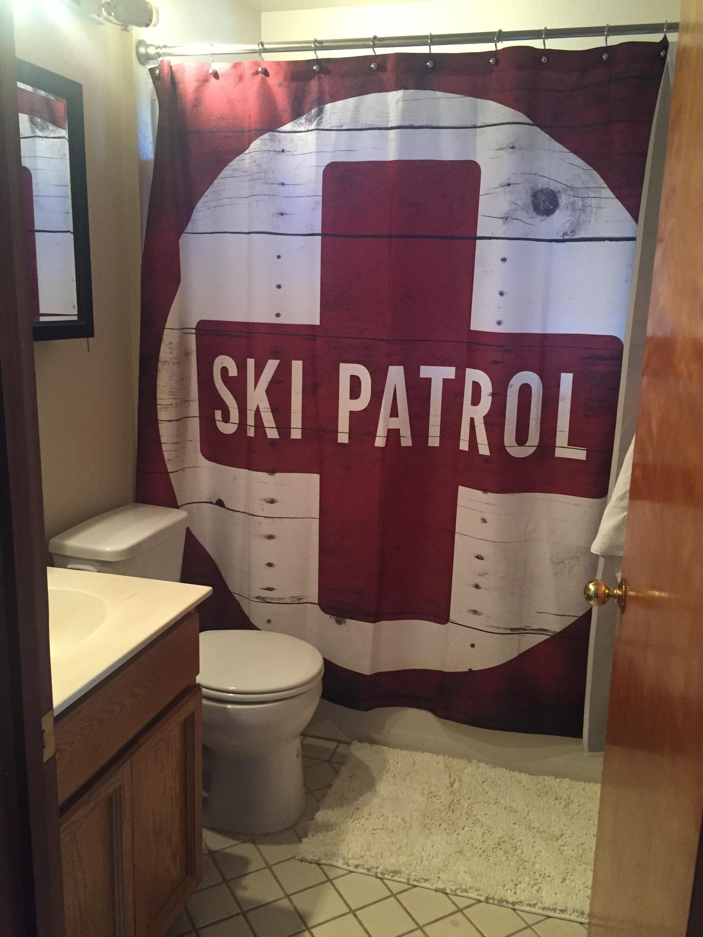 Ein Badezimmer mit einem roten und weißen Duschvorhang im Ski-Rettungsteam-Design, einer weißen Toilette und einem Holzkabinent.
