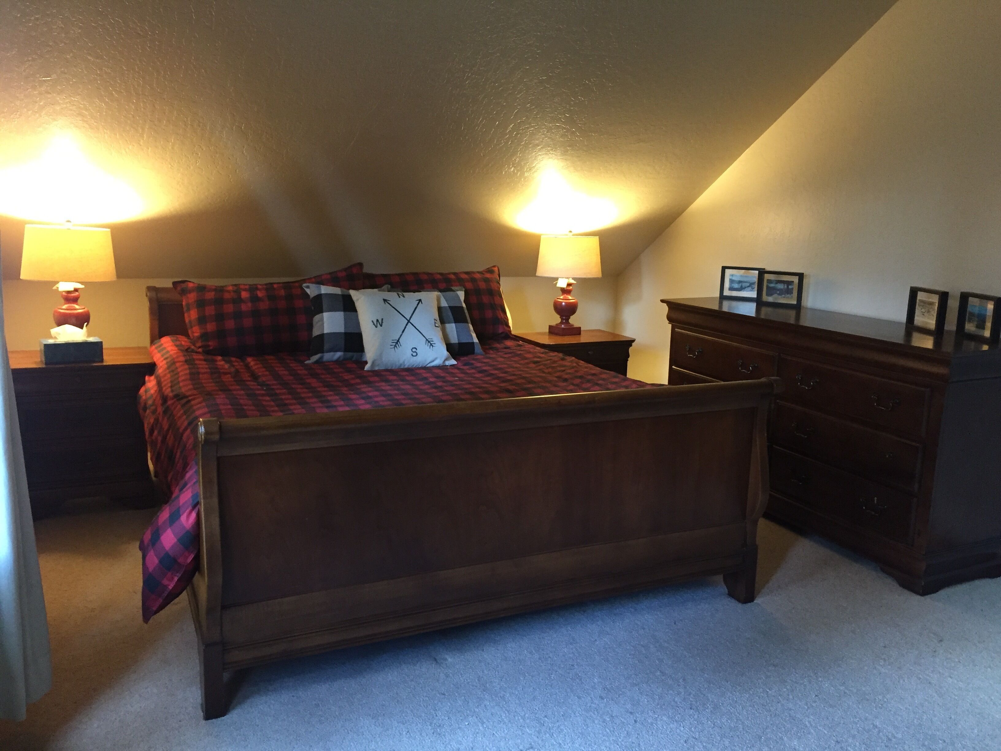 A bedroom with a wooden bed, two bedside tables with lamps, a dresser, and a sloped ceiling.