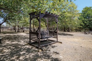 A wooden swing set in a park with a fenced area and trees. - Double U Barr Texan | Cabin with Creek Access (Bandera)