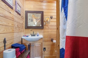Baño de cabaña de madera con lavamanos, espejo y toallero.