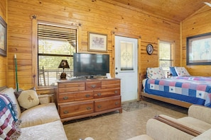 Un interior de cabaña acogedor con piso de madera, un televisor en una cómoda, una cama con colcha y una puerta decorada con una estrella.