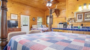 Ein gemütliches Blockhaus-Interieur mit einem großen Bett, einem Fernseher, einer Holzbalkendecke und einem aufgehängten Tierkopf.