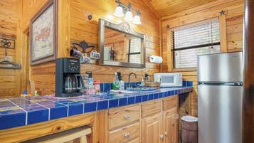 A wooden cabin interior with a kitchen featuring a coffee maker, microwave, and refrigerator.