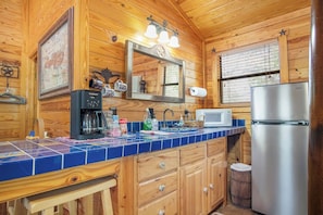 Interior de una cabaña de madera con cocina equipada con cafetera, microondas y refrigerador.