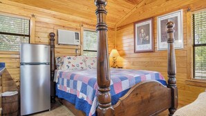 Ein Schlafzimmer einer Holzhütte mit Bett, Kühlschrank und einem Fenster mit Jalousien.