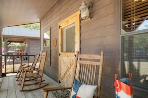 A wooden porch with rocking chairs and a door with a window. - Double U Barr Texan | Cabin with Creek Access (Bandera)