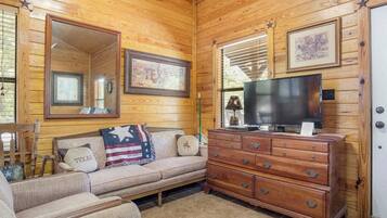 A cozy room with a wooden ceiling, a sofa with a Texas-themed pillow, a television on a wooden dresser, and framed pictures on the walls.