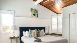 A bedroom with a large bed, two bedside tables, a ceiling fan, and a window with blinds.