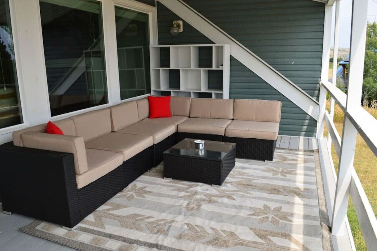 Un espace extérieur aménagé, abrité, avec un canapé d’angle, une table basse et un tapis à motifs.