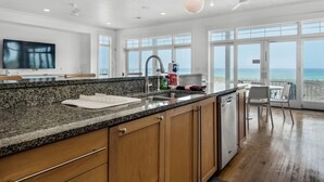 A modern kitchen with granite countertops, wooden cabinets, and a large window overlooking the beach.