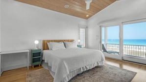 A bedroom with a bed, a nightstand, a ceiling fan, and a view of the beach.