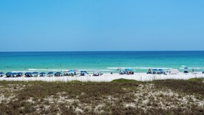 A beach with white sand, clear blue water, and a grassy foreground.