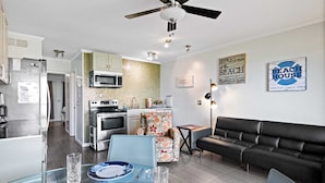 A modern kitchen with a microwave, oven, and refrigerator. There is a dining area with a table and chairs, and a black leather sofa. - Ocean view, unique, stylish, contemporary, upscale condo with a modern ambiance (Hilton Head Island)