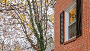 A brick house with a stone retaining wall, a small garden with steps leading to the door, and a tree with yellow leaves. - Remodeled, Updated, Perfect Location Next to Downtown/PSU! (State College)