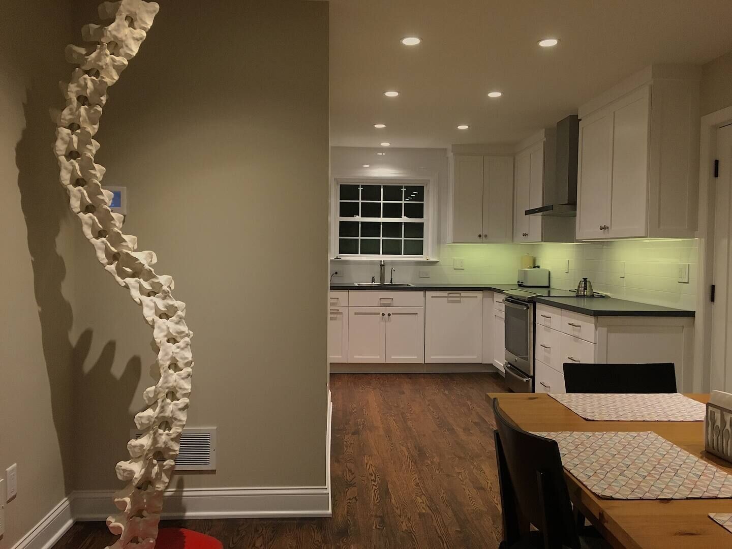 A modern kitchen with white cabinets, a wooden dining table, and a unique white sculpture on the wall.