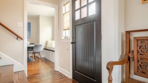 A hallway with a dark wooden door, a staircase, and a dining area with a table and chairs. - Remodeled, Updated, Perfect Location Next to Downtown/PSU! (State College)