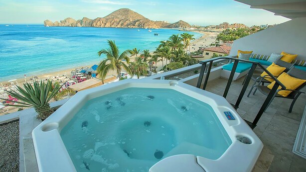 Een jacuzzi op een balkon met uitzicht op een strand, palmbomen en een berg in de verte.
