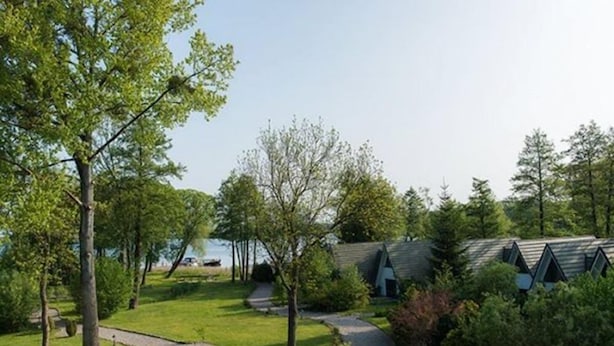 Uma pousada à beira do lago com um gramado, caminhos para passear e cabanas com telhados inclinados.