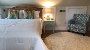 Ein Schlafzimmer mit einem großen Bett, einem Nachttisch mit Lampe, einem Sessel und einem flauschigen Teppich.