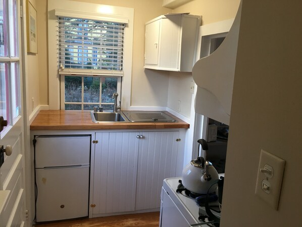 A compact kitchen with a wooden countertop, a built-in sink, a refrigerator, and a stove. - Cozy Cottage in Historic Lewes Delaware (Lewes)