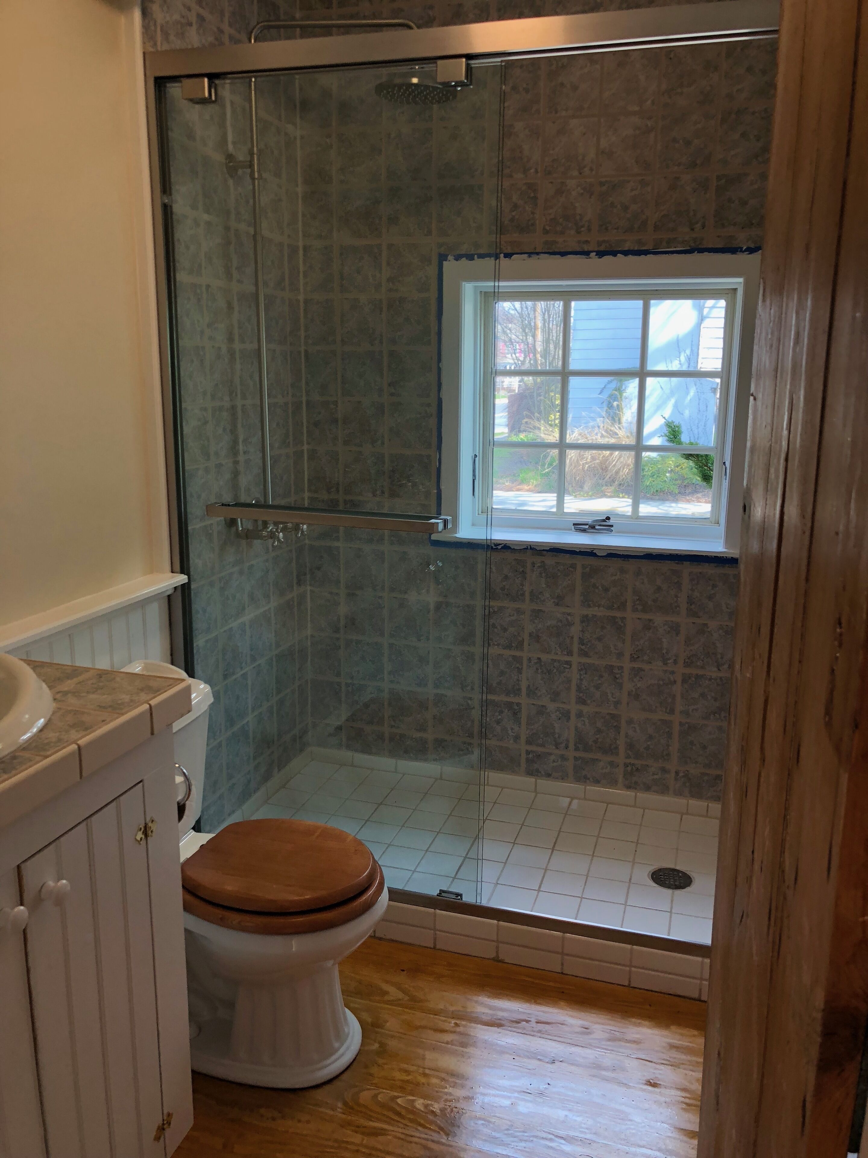 A bathroom with a glass-enclosed shower, a toilet, and a window.