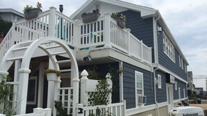 A two-story house with a balcony, white railings, and a garage with a Johnson boat. - LBI Bayfront Beauty Brand New Hot Tub! Boat Slip Included! Two blocks to Beach! (Ship Bottom)
