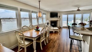 A spacious dining area with a view of the water, a fireplace, and a television mounted above it. - LBI Bayfront Beauty Brand New Hot Tub! Boat Slip Included! Two blocks to Beach! (Ship Bottom)