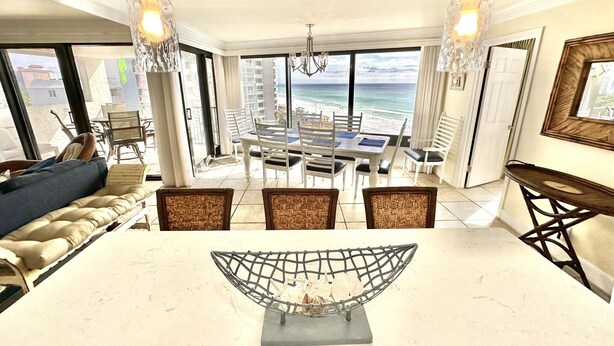 Un vaste espace dédié à la salle à manger, offrant une vue sur la plage, agrémenté d’un lustre et d’une composition florale moderne en guise de centre de table.