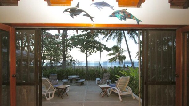 Vista attraverso una porta di vetro su un patio con mobili da esterno, palme e vista sull'oceano.